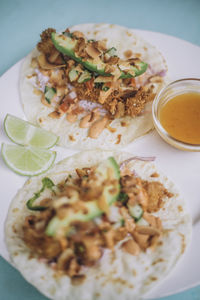 High angle view of fresh tacos with lime slices and sauce on table