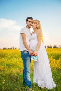 Portrait of couple holding baby shoes while standing on field