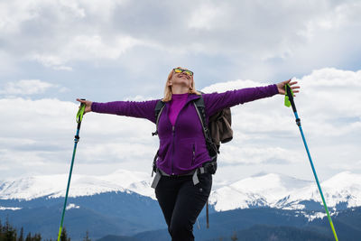 Low angle view of young woman standing on mountain against sky