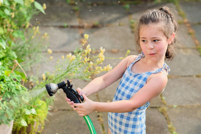 Young girl is watering plants in the backyard while wearing a bathing suit