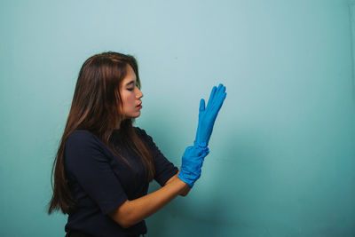 Young woman holding blue while standing against wall