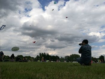 People photographing hot air balloons flying over field against sky