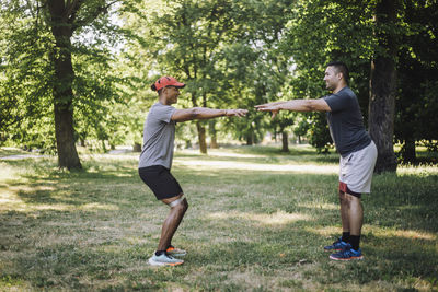 Side view of male friends exercising together on grass at park