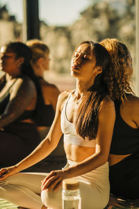 Female friends exercising while sitting back to back in yoga class