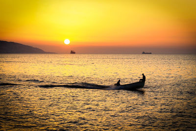 Scenic view of sea with people in boat against sky during sunset