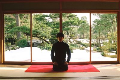 Portrait of young man exercising while kneeling against window