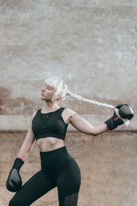 Portrait of woman with boxing gloves standing against wall