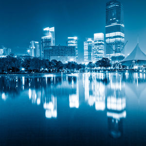 Reflection of illuminated buildings in lake against blue sky