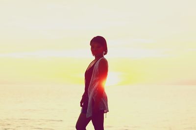 Woman standing at beach against sky during sunset