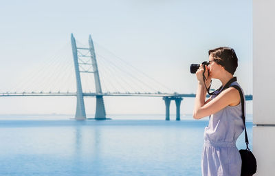 Woman photographing on bridge against sky