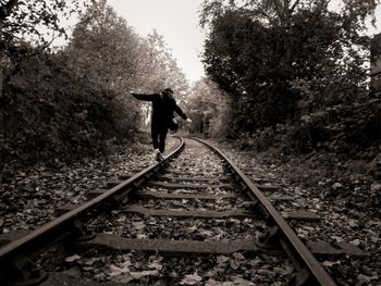 Rear view of teenage boy with arms outstretched walking on railroad track