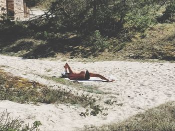 Shirtless man lying on sand during sunny day