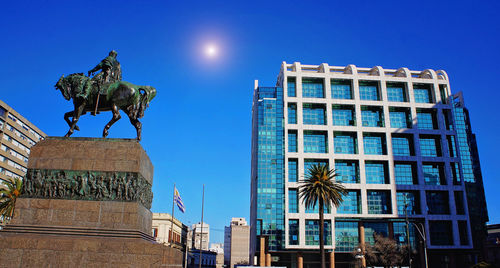 Low angle view of statue against buildings against blue sky