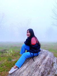 Young woman sitting on field during foggy weather