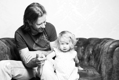 Father with little daughter sitting on sofa at home