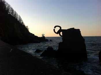 Silhouette rocks on beach against sky during sunset