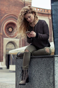 Young woman sitting on sidewalk in city