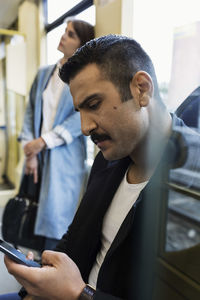 Young man using mobile phone while woman standing in tram