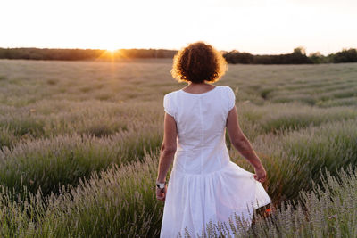 Rear view of woman standing on field against sky during sunset