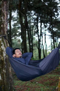 Young man relaxing on tree trunk in forest