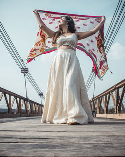 Low angle view of woman standing by bridge against sky