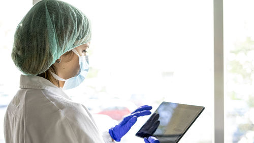 Cropped shot of an unrecognizable female nurse using a digital tablet while standing in a hospital. whit a mask