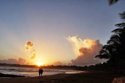 Silhouette people standing on beach against sky during sunset