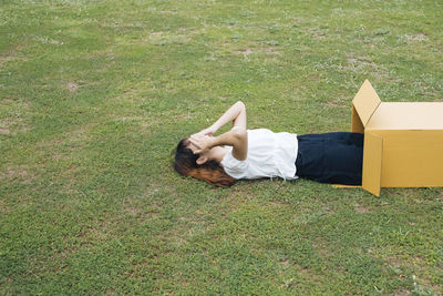 Woman lying on grass in cardboard box