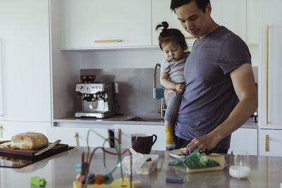 Father with food carrying male toddler by kitchen counter