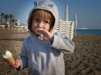 Thoughtful little girl wipes her mouth with back of her hand while eating ice cream on a sea beach