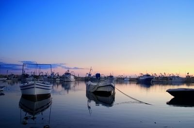 Boats moored in harbor at sunset