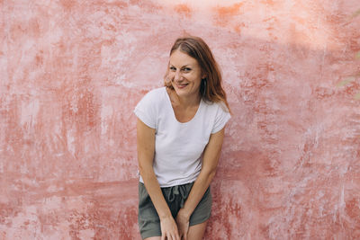 Young woman in front of a coral coloured wall laughing at the camera in tulum, mexico