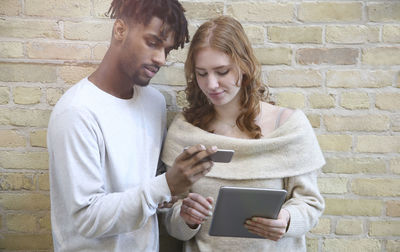 Young man using mobile phone against brick wall