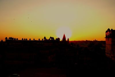 Silhouette people by buildings against sky during sunset