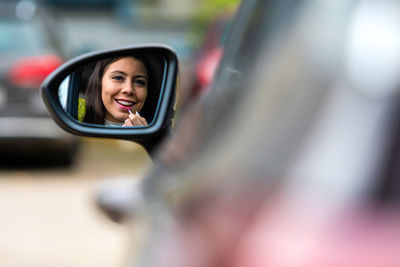 Portrait of smiling woman applying lipstick reflecting in mirror