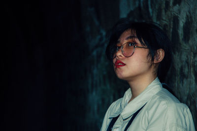 Portrait of young woman looking away while standing against wall