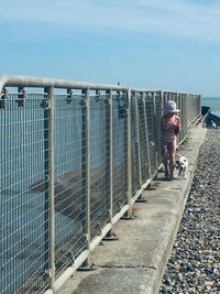 Full length of girl with dog walking on footpath at beach