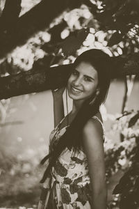 Portrait of young woman standing against tree