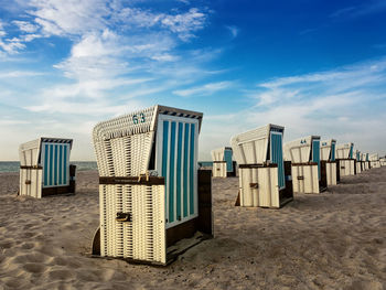 Hooded beach chairs on sand at beach against cloudy sky