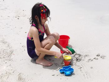 Girl playing with toys while crouching on sand at beach