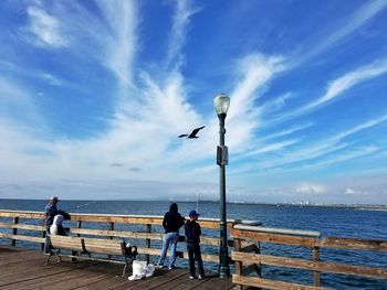 Scenic view of sea with people fishing from pier against sky