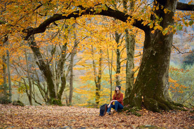 Man sitting by tree in forest during autumn