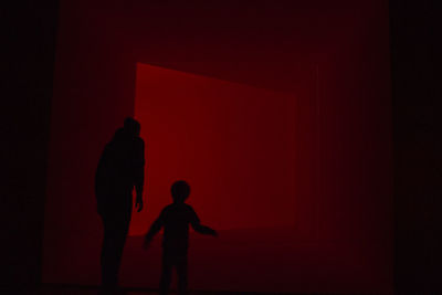 Silhouette boy standing against red wall