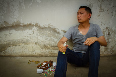 Mature man sitting by narcotics against wall