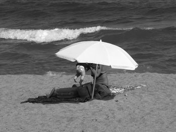 High angle view of mother and child below parasol at sandy beach