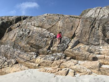 Full length of girl climbing on rock formation against sky