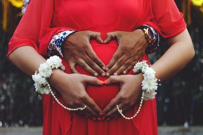 Pregnant woman and man making heart shape with hands on her stomach