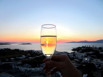 Cropped image of hand holding champagne flute at mykonos during sunset