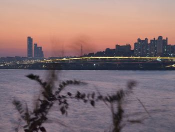 Scenic view of river by buildings against sky during sunset