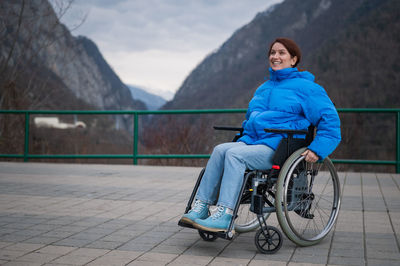 A woman in a wheelchair on a point view admires the high mountains. thrust to life